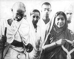 Mahatma Gandhi walking with a staff, Sarojini Naidu beside him in a bordered sari, with other figures behind.