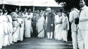 A public ceremony photographed from a distance, with a crowd in white clothing gathered under an awning.