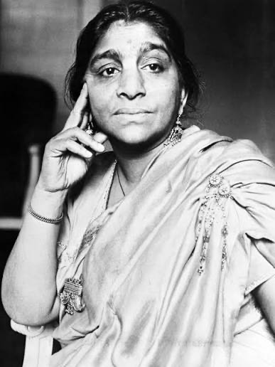 Black and white portrait of Sarojini Naidu seated with her chin resting on her hand, wearing a pale sari.
