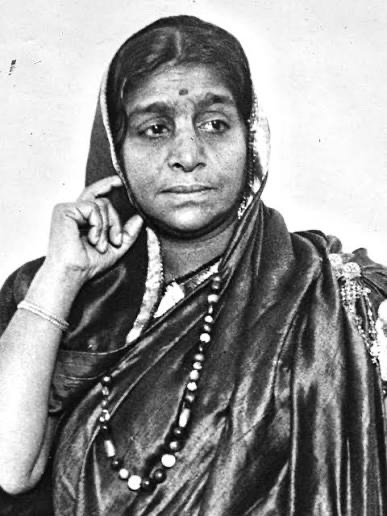 Portrait of Sarojini Naidu in a dark silk sari with a long beaded necklace, one hand raised to her cheek.